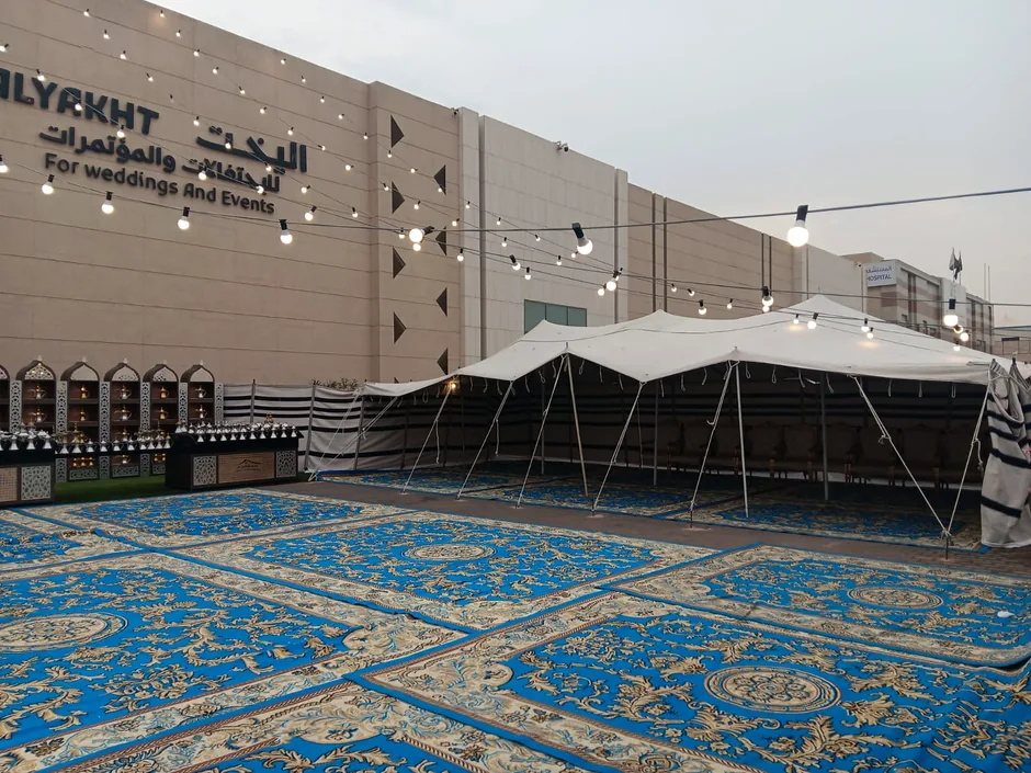 سجاد أزرق واسع بجانب خيام المناسبات في ساحة خارجية