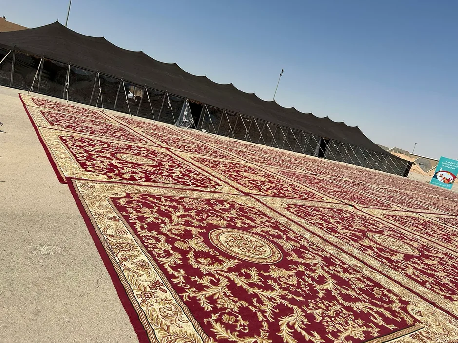 سجاد أحمر كبير مفروش قرب خيام في موقع صحراوي