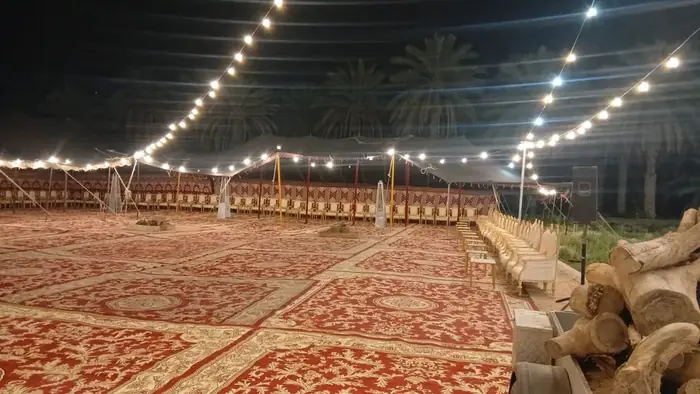 خيمة استقبال واسعة في المساء مع سلاسل إنارة وسجاد أحمر ومقاعد ضيافة