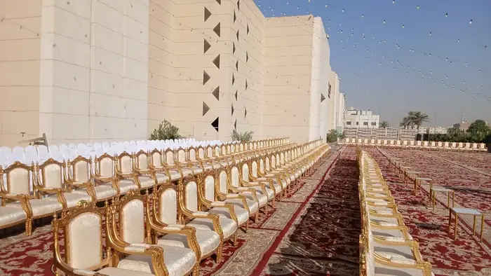 صفوف طويلة من الكراسي الذهبية بكسوة بيضاء على سجاد أحمر في مناسبة خارجية